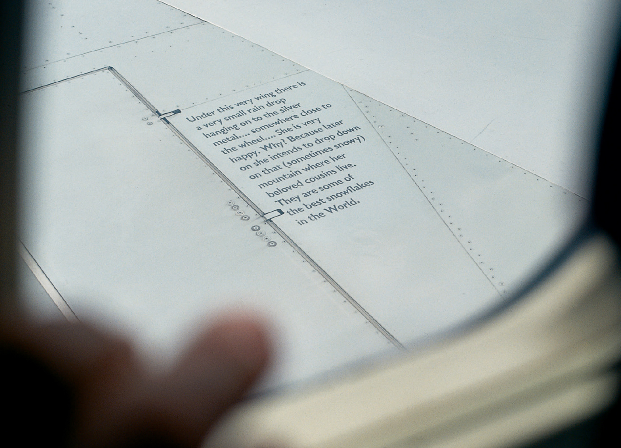 A photograph of text on the wing of an airplane explaining that a raindrop on the plane will be happy to drop and join its friends in the mountains.