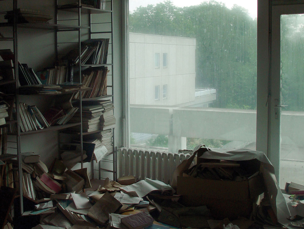 A photograph of office bookshelves with books piled on the ground.