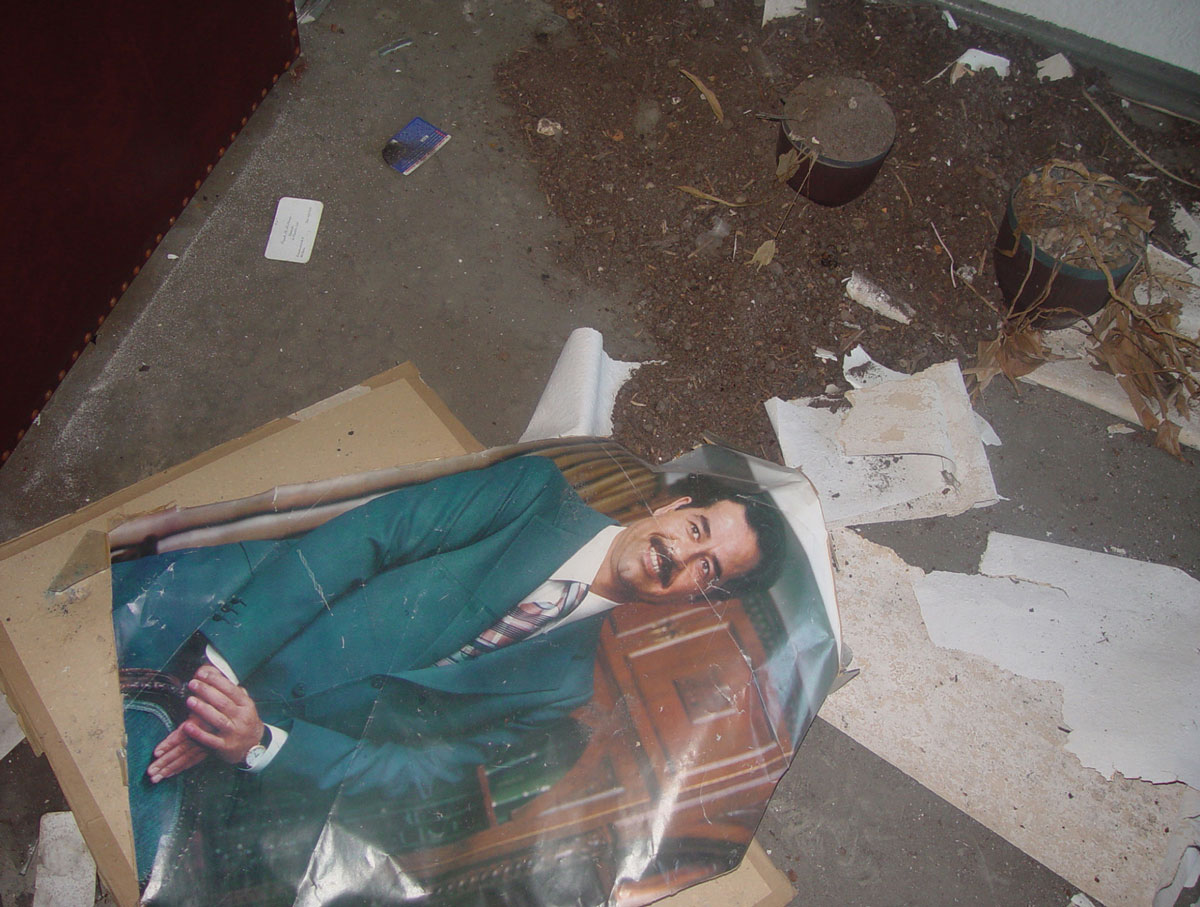 A photograph of a smiling man in a suit left on the ground, near a pile of dirt.