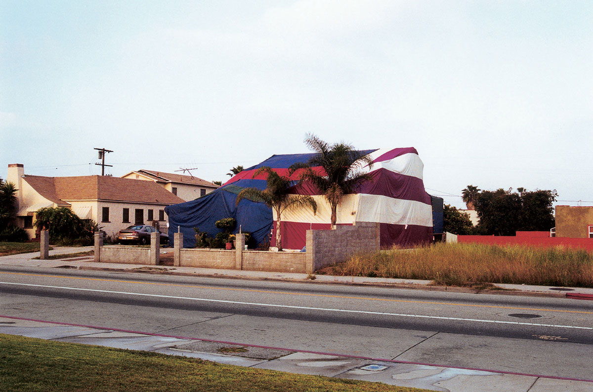 Artist Susan Silton’s photograph of a house enveloped in striped tarpaulin.