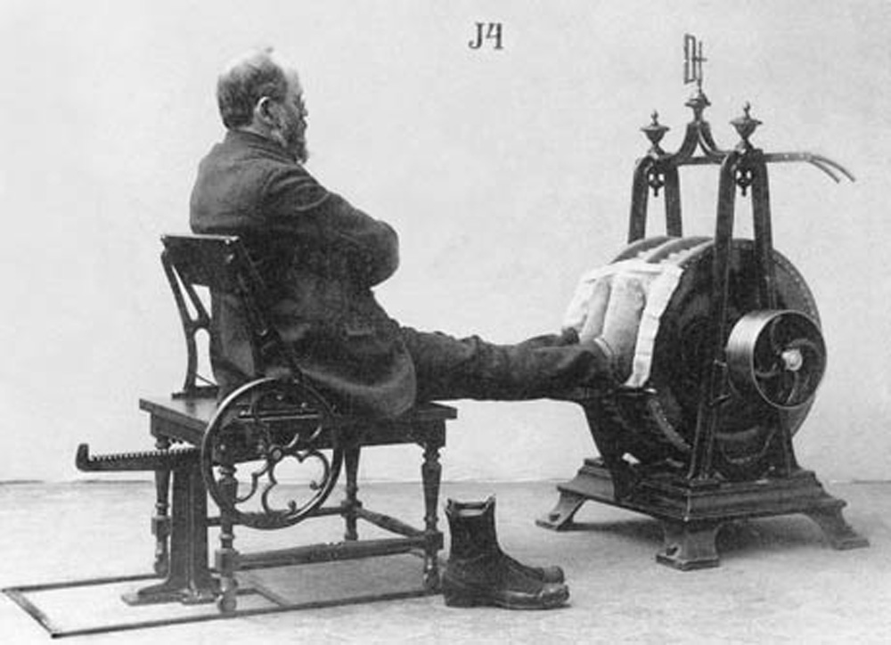 A nineteen-eighties photograph of a man in a suit sitting in a chair with his feet up on a Zander exercise machine.