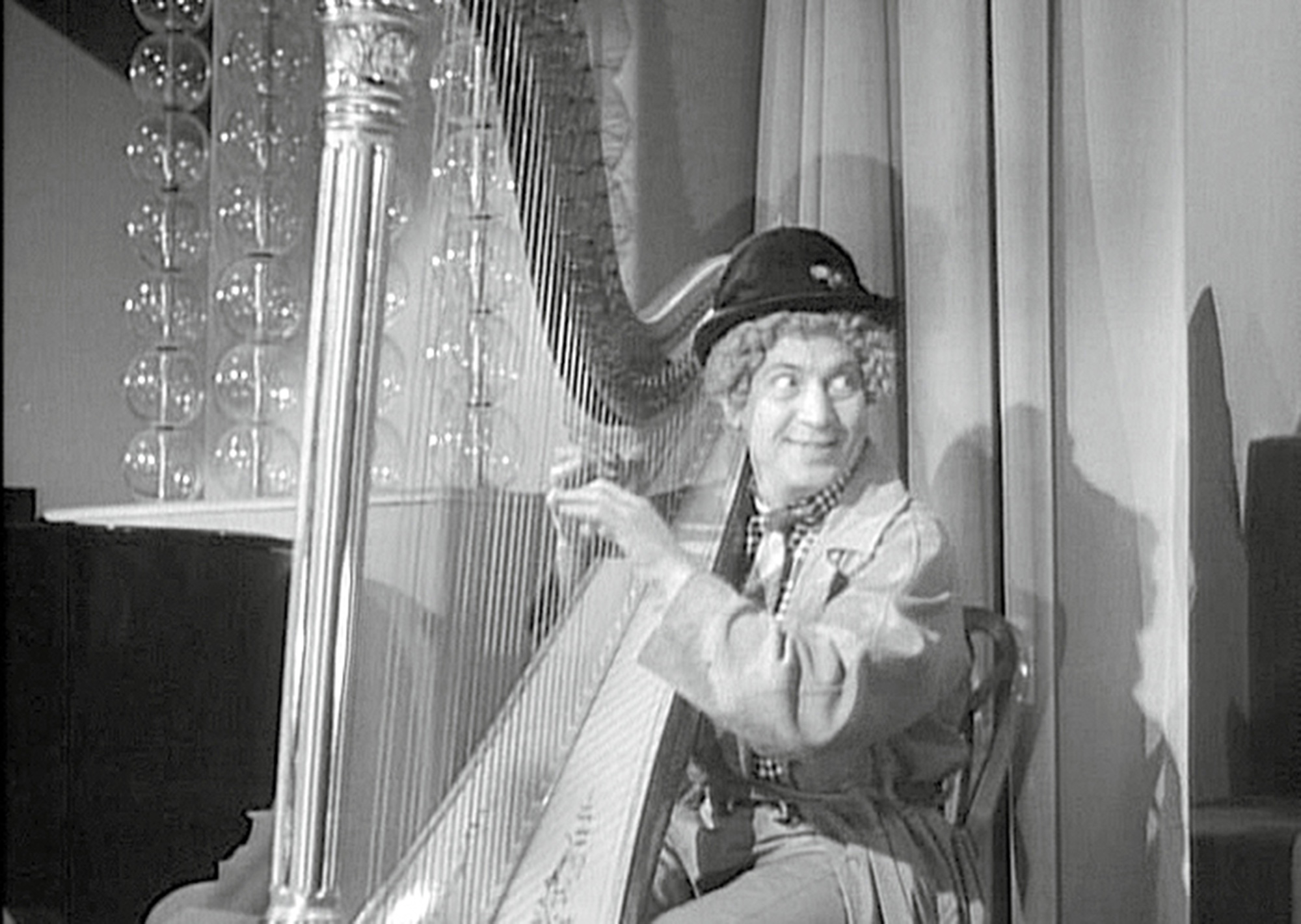 A still from the nineteen forty one film “The Big Store” depicting Harpo Marx playing the harp in front of decorative glass balls.