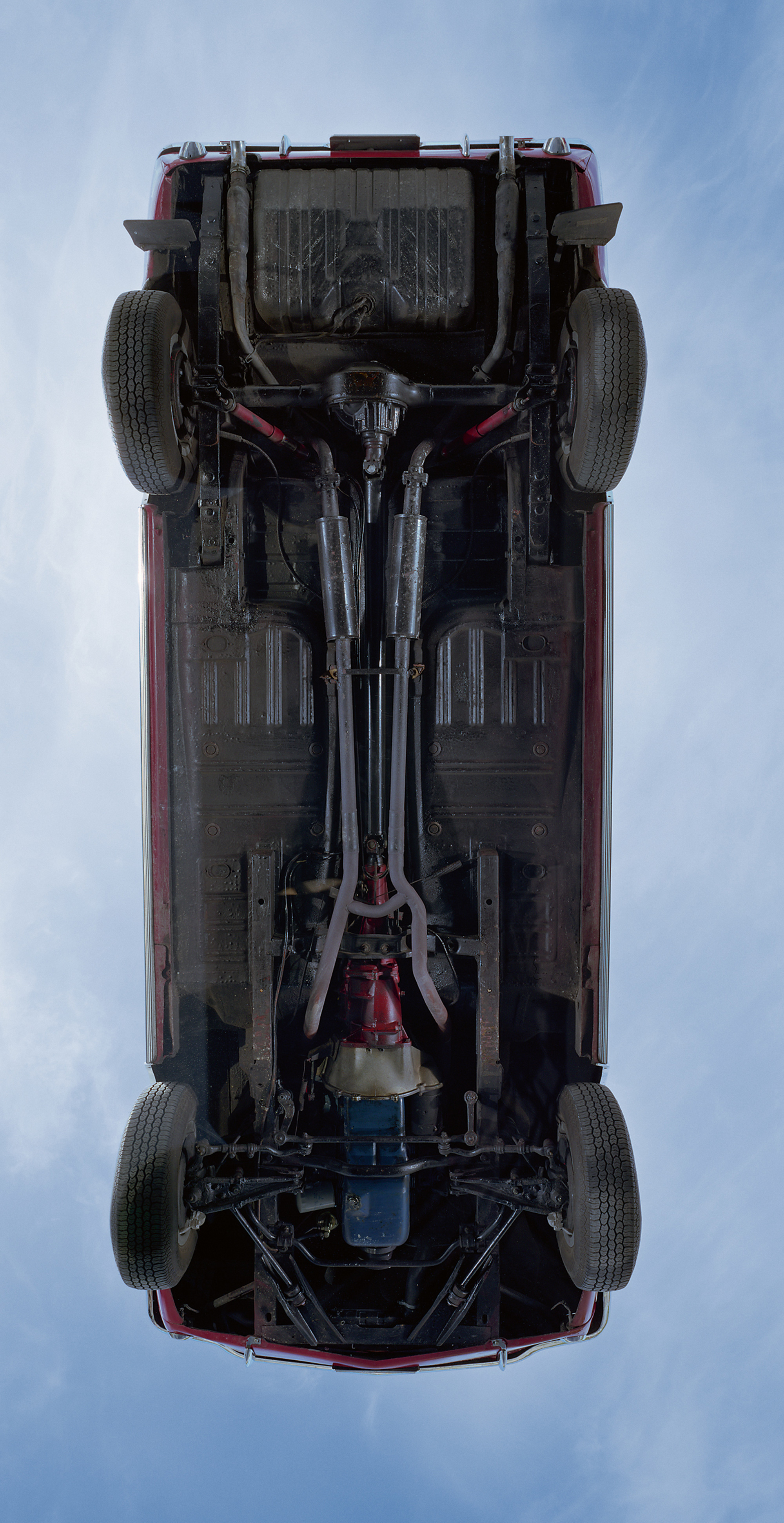 A photograph of the underbelly of a car resting on a large sheet of heavy-duty glass. 