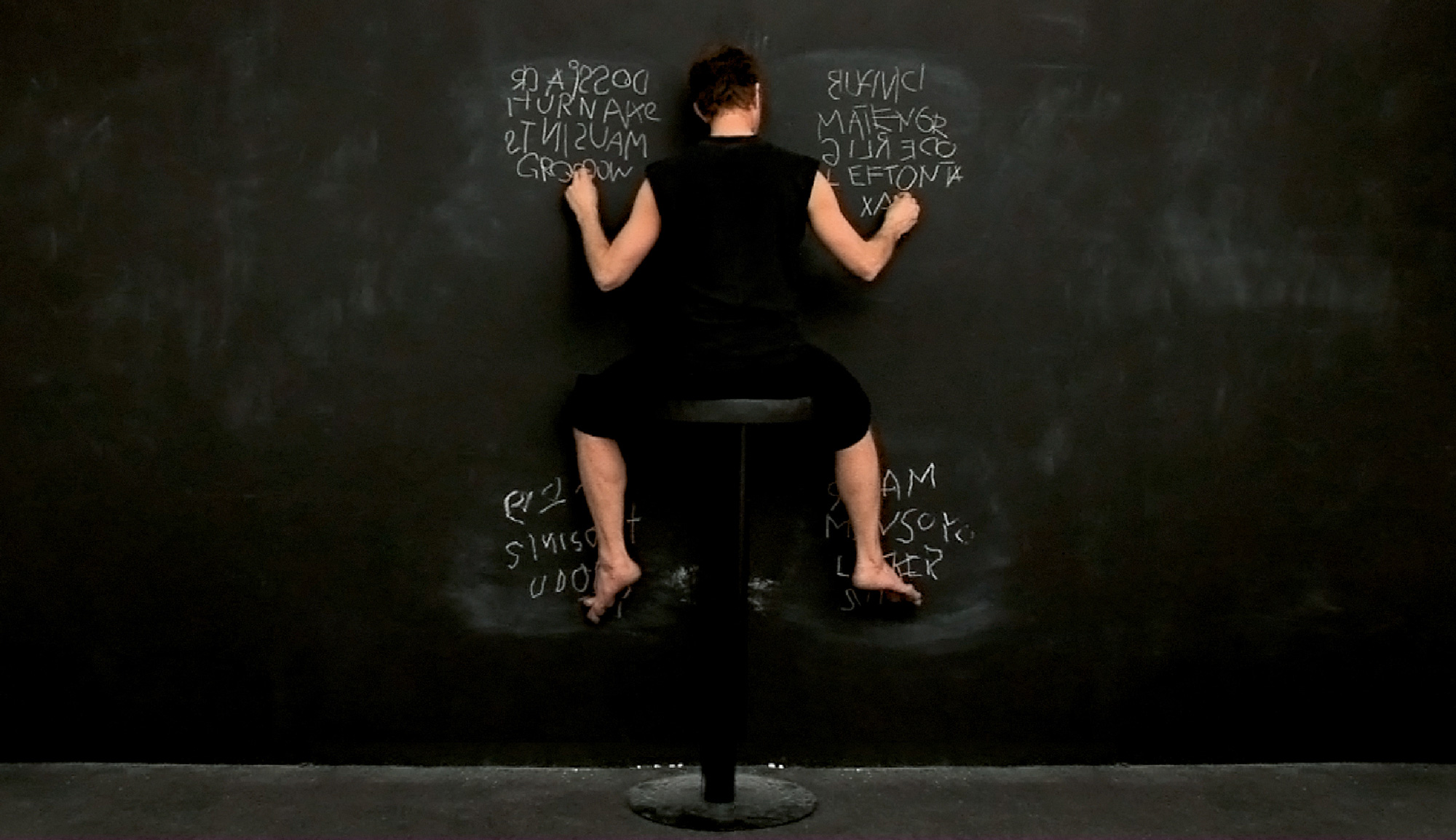 A photograph of a woman writing on a chalkboard using all four limbs. 