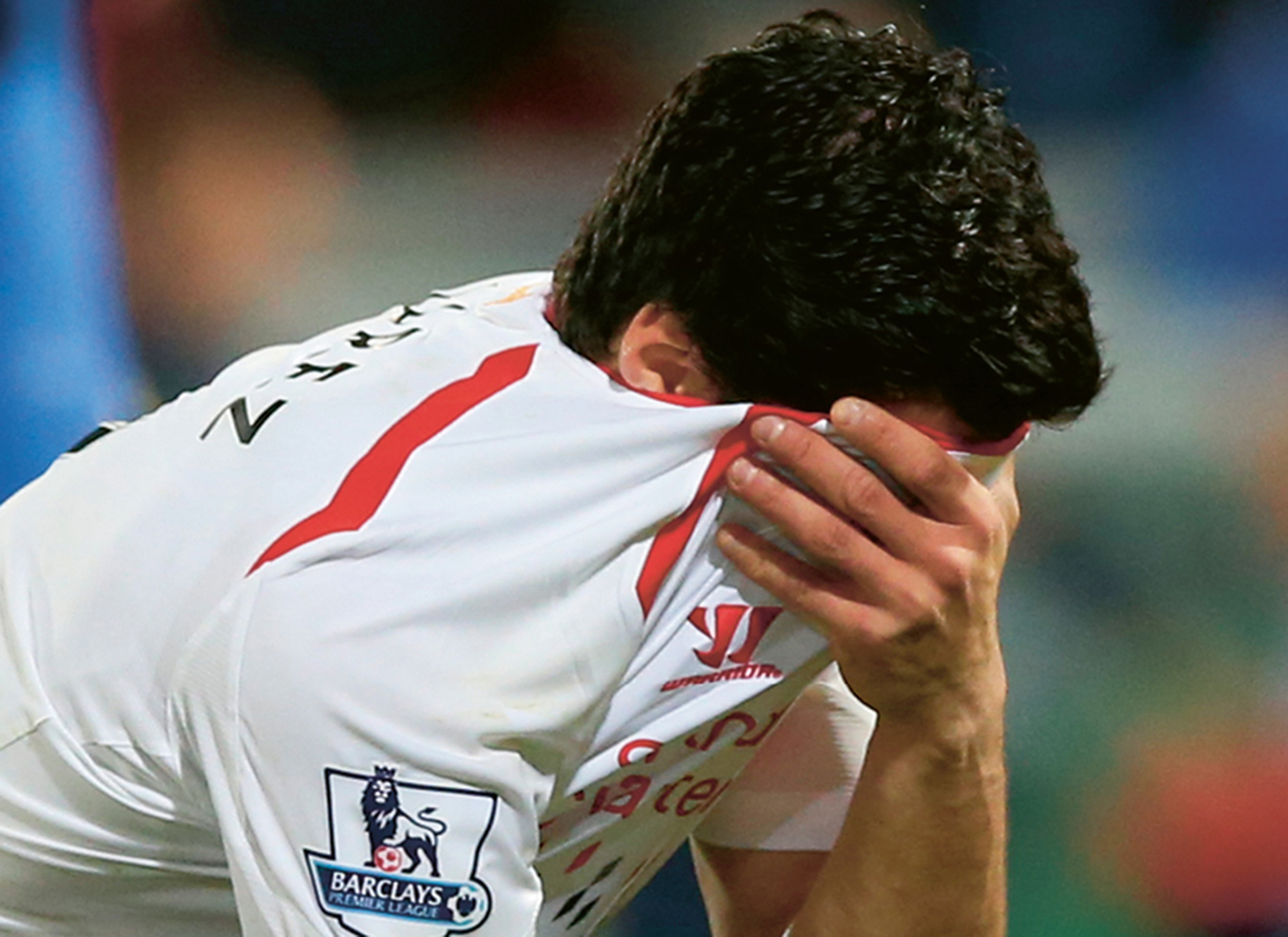 A photograph of soccer player Luis Suárez hiding his face in his jersey.