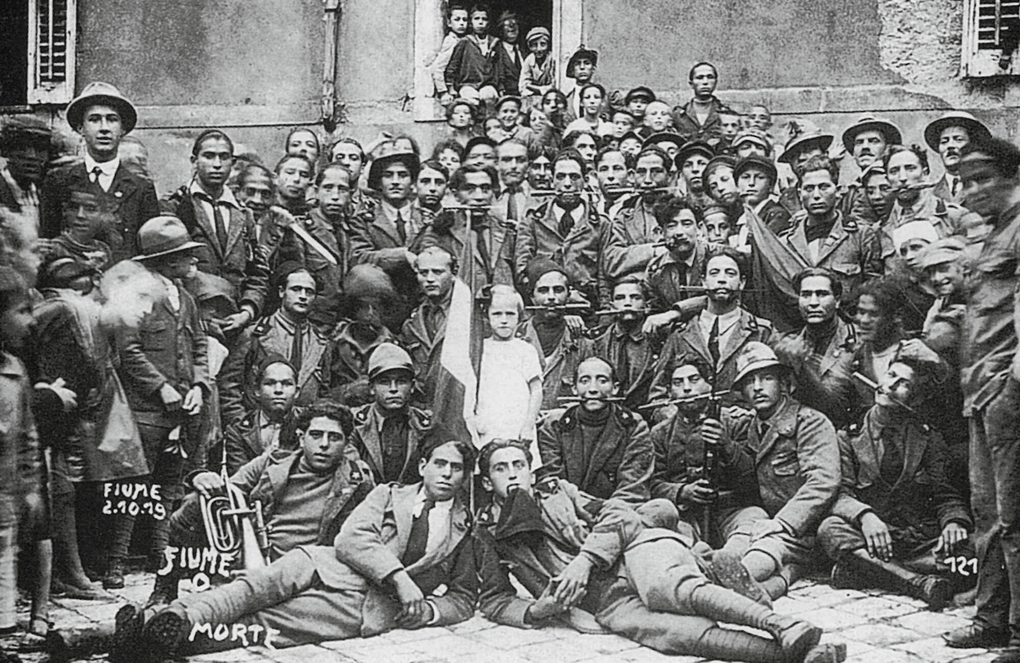 A nineteen nineteen photograph of a group of arditi in Fiume. The men can be seen holding daggers between their teeth, a practice these soldiers favored on the battlefield which became a symbol of their fighting spirit.