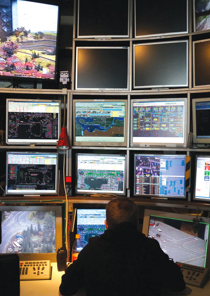 A photograph of a Miniatur Wunderland employee overseeing monitors backstage.