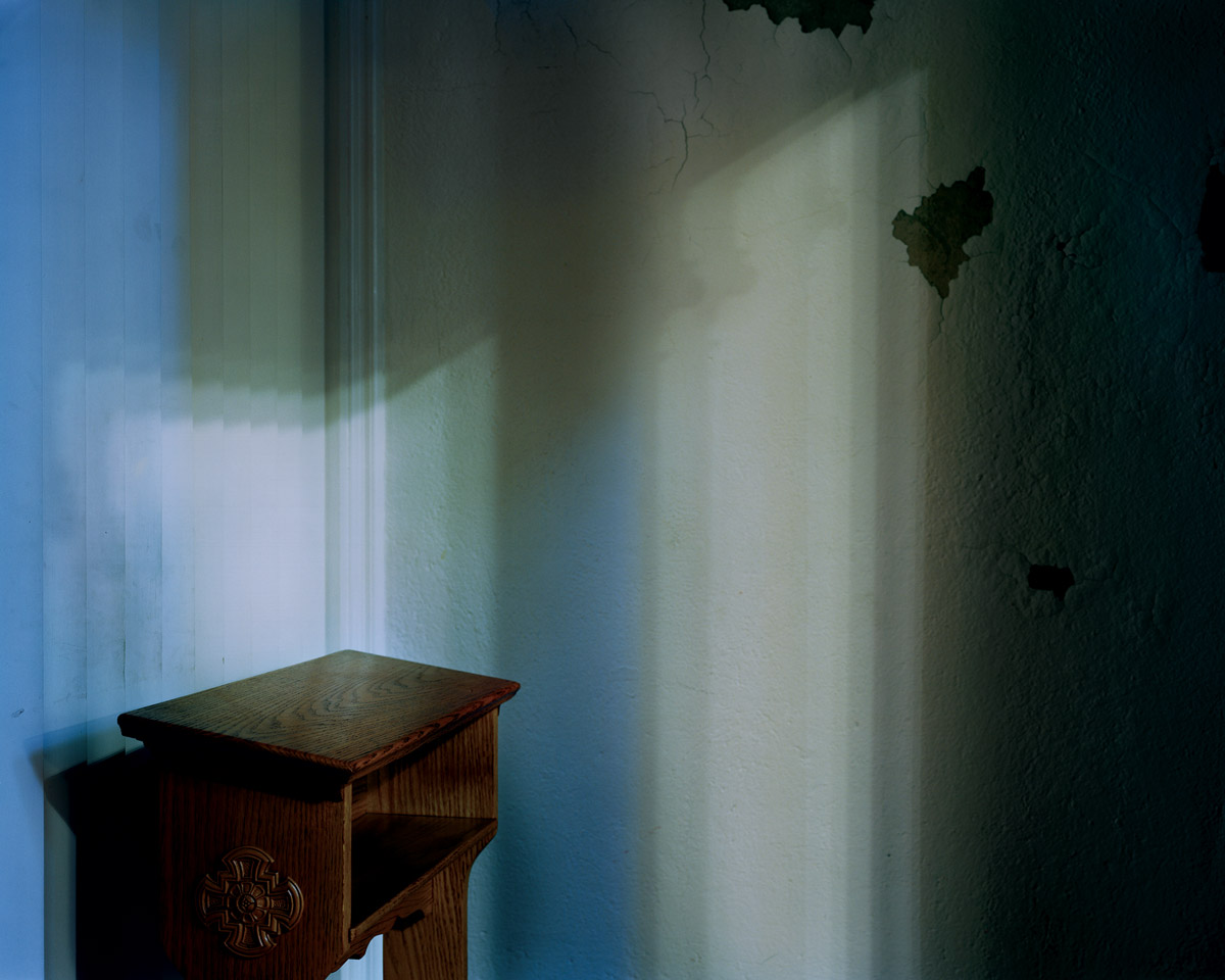 A photograph of the inside of a confessional booth, with a wooden stand and blue walls, which the artist associates with Saint Pancras.