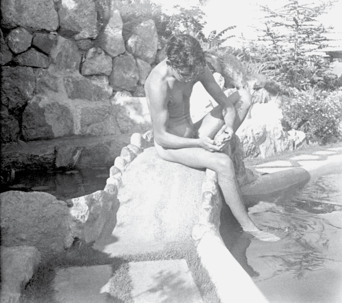 A nineteen twenty eight to twenty nine photograph by Murnau of David Rollins at Wolf’s Lair. Rollins is posed with his hands tending to his foot crossed over his knee, in the manner of the subject of the antique sculpture “Boy with Thorn.”